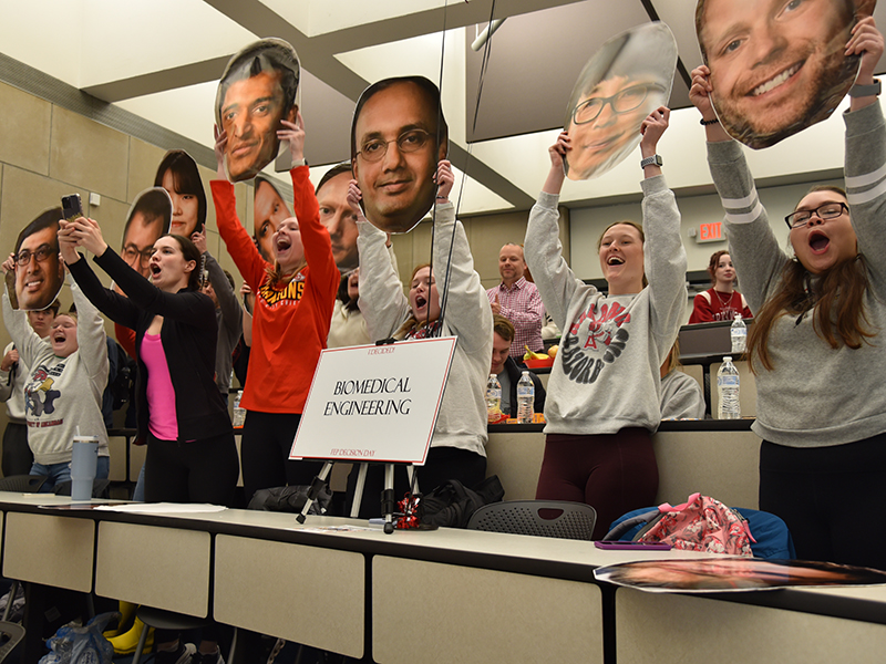 Biomedical engineering students hold up printed faces of faculty members