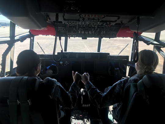 Photo of Cadets Manon and Niles giving a fist bump inside the cockpit of a C-130 plane.