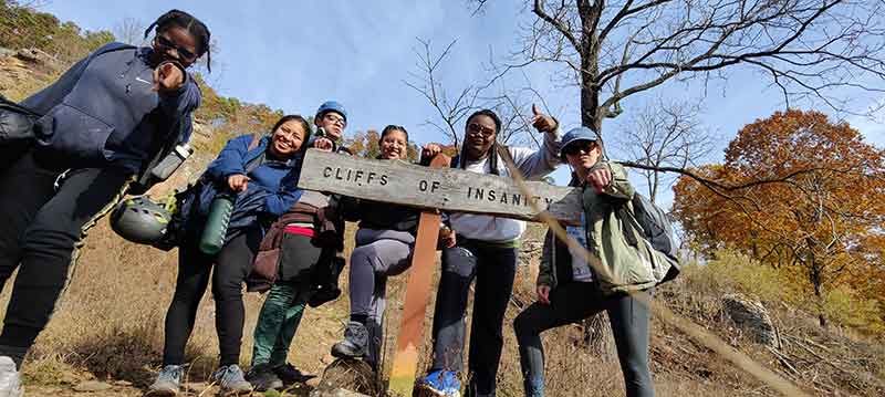 Hikers pass a sign that reads Cliffs of Insanity