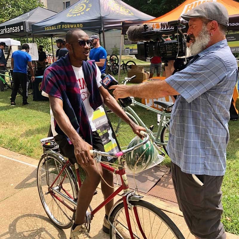 A photographer for a local television station interviews Victor Onwukwe about his bicycle.