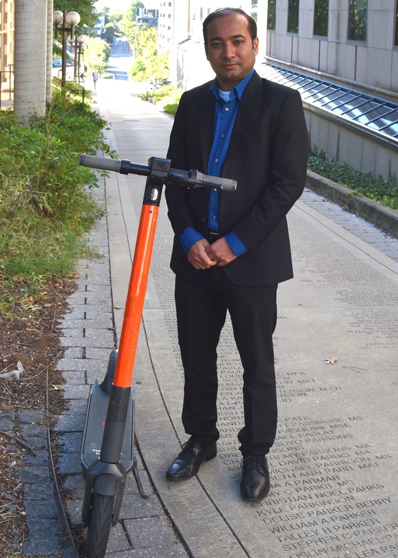 Suman Mitra, assistant professor of civil engineering, poses with an e-scooter similar to the types of scooters that will be deployed in several Fort Smith neighborhoods as part of a research study to begin in January.