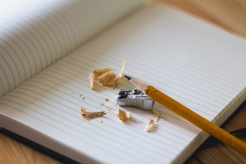 An open notebook with a sharpened pencil and pencil shavings on the top page.