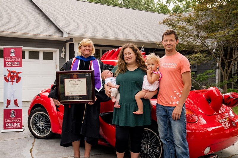 Jan Emory, left, presents a framed diploma June 27 to Star Lowrey-LaGrone, pictured with her husband, Toby, and children, Atlas and Aspen, at her Fort Smith home.