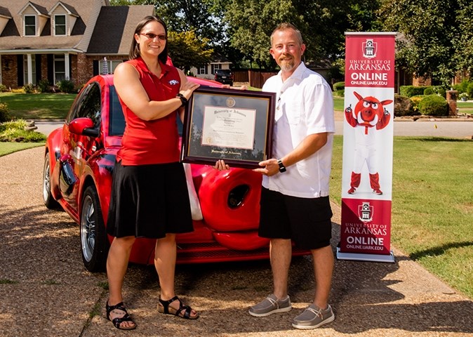Jason Rose receives a framed diploma for his master's degree in engineering management from Megan Whobrey of the College of Engineering at the U of A. The presentation took place July 1 at Rose's home in Fort Smith as part of the RazorBug Diploma Tour.