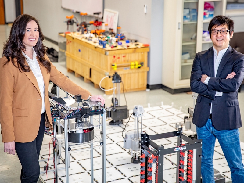 Michelle Barry and Wenchao Zhou in the AMBOTS lab, in front of a robotic 3D printing platform.