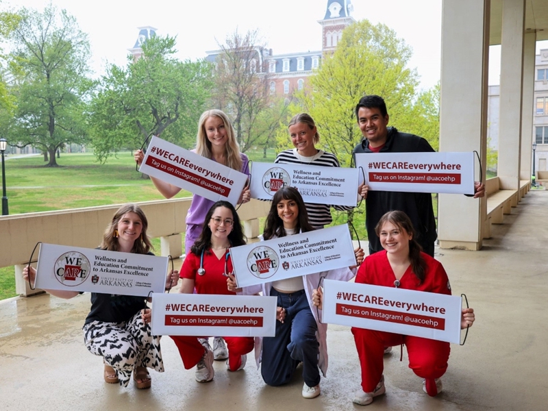 Students from the College of Education and Health Professions pose with WE CARE banners. Members of the University community, friends and alumni are encouraged to take a photo with the banner while out and about this summer and post it on social media using the hashtag #WECAREeverywhere.